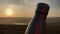 Close-up of steel thermo bottle with cap on background of sunset.