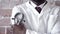 Close up of stethoscope in hand, held up by a black male doctor standing in a white lab coat against a red brick wall