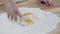 Close-up of stirring eggs into a pile of flour on the wooden table and kneading the dough