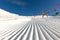 Close-up straight line rows of freshly prepared groomed ski slope piste with bright shining sun and clear blue sky