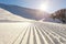 Close-up straight line rows of freshly prepared groomed ski slope piste with bright shining sun and clear blue sky background.