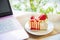 Close up strawberry crepe cake on a white plate next a pink laptop with silicon dust keyboard cover folded on white table next a