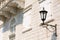 Close-up of a street lamp on the wall of a house under a balcony on a sunny day.