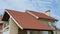 A close-up on a stucco house with a red metal tiled double gabled roof, a chimney, fascia boards, rain gutters, two satellite dish