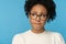 Close up studio portrait of shy awkward young Afro American woman wear glasses white sweater, biting lips feeling embarrassed,