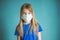 Close-up studio shot of a lovely blonde little girl in a blue t-shirt and medical mask posing against a blue background