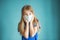 Close-up studio shot of a lovely blonde little girl in a blue t-shirt and medical mask posing against a blue background. Surprised