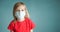Close-up studio shot of a lovely blonde little girl in a red t-shirt and medical mask posing against a blue background. Copy space