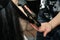 Close up of stylist hands with styling iron straightening woman hair at salon