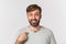 Close-up of surprised handsome man with beard, pointing at himself and smiling, standing over white background