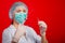 Close-up of a syringe with a stream of medicine from a needle in the hands of a female doctor on a red background.