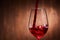 Close-up of tasty red wine pouring in the pure fragile wineglass standing against wooden background.