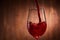 Close-up of tasty red wine pouring in the pure fragile wineglass standing against wooden background.