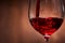 Close-up of tasty red wine pouring in the pure fragile wineglass standing against wooden background.