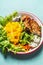 Close up of tasty salad bowl with roasted chicken breast and mango with cutlery on light blue background