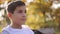 Close up of Teenage boy in white sweater sitting on the bench. Handsome school boy with backpack in autumn park