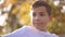 Close up of teenage boy in white sweater sitting on the bench. Handsome school boy with backpack in autumn park