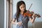 Close up of teenage girl learn to play a violin instrument beside the window