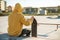 Close-up of a teenager dressed in a jeans hoodie sitting in a skate park and holding a skateboard