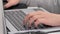 Close-up of a teenager\'s hands typing on a laptop keyboard at an office desk. Unrecognizable teenager working on