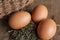 Close-up of three farm eggs on hay and wicker basket on wooden table