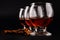 Close up of three goblet glasses in a row with cognac, dark rum or brandy and scattered cinnamon sticks on a black background with