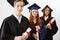 Close up of three happy mixed race international college graduates smiling rejoicing holding diplomas over white