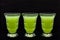Close up of three vintage etched shot glasses with healthy organic green drinks on black background with space for text