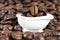 Close-up of a tiny white bathtub full of coffee beans surrounded by scattered roasted beans.