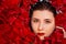 Close-up, top view, beauty portrait, face of a young woman in a bath with water and floating red rose petals and rosebuds.