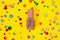 Close up top view on the bottle with silvered pink nail polish or glitters on bright yellow background with multicolored