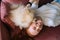 Close-up top view of cute white small Spitz pet dog lovely licking face of laughing young woman lying on comfortable