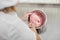 Close up top view of hands of female confectioner in white hat and uniform, mixing red cream in the bowl with spatula