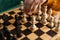 Close-up top view of hands unrecognizable woman making chess move sitting at table in dark room, selective focus.