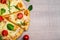 Close up top view of pizza with tomatoes and herbs over wooden table