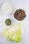  close up top view shot of a bowl of sliced beef fillet pieces, a plate of cellophane glass noodles, a cup of Vietnamese