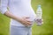 Close-up of torso of pregnant woman holding bottle of water outs