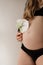 Close-up of torso of young pregnant model standing with calla flower in home on white background