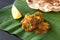 Close up traditional Indian butter chicken curry and lemon served with chapati bread on banana leaf