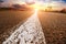 Close-up of a traffic line on an empty road with a forest and sky with sunset on the background