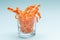 Close-up transparent glass with homemade healthy longitudinal carrot chips on gentle blue background.