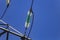 Close up of a transparent turquoise high voltage insulator or isolator in sunlight on electric tower on blue sky background.