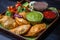 Close-up of a tray of assorted empanadas with different fillings and a side dish of fresh salsa and guacamole