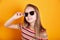 Close-up of trendy little girl in summer clothes and sunglasses on yellow background
