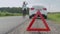 Close up on triangle warning sign with woman calling for assistance after breaking down with her car on background