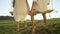 CLOSE UP Two barefoot kids sitting on wooden swing holding hands at sundown