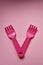 Close-up of two childish plastic pink forks on a pale pink background. Dishes for a picnic