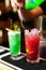 Close-up of two colorful red and green cocktails with lime and brown sugar in bar, blurred background.