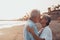 Close up of two cute and happy seniors having fun and enjoying together a sunset day at the beach. Mature couple in love kissing