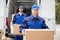 Close-up Of Two Delivery Men Carrying Cardboard Box